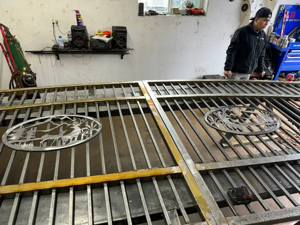 Custom arched driveway gates with plasma-cut deer scene medallions under fabrication