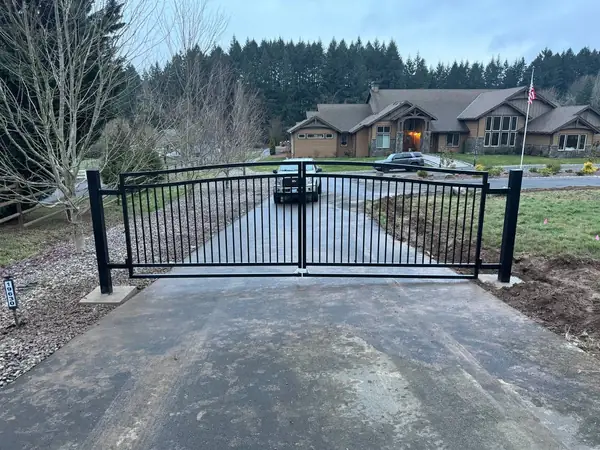 Arched black iron double driveway gate in front of a custom craftsman home