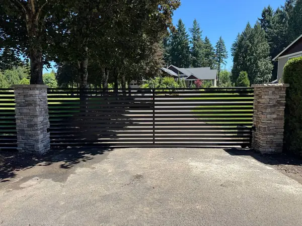 Modern black horizontal-slat automatic sliding gate between stacked-stone pillars at a residential driveway
