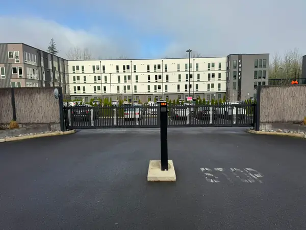 Black bi-parting slide gate closed in front of Casey apartments with bollard