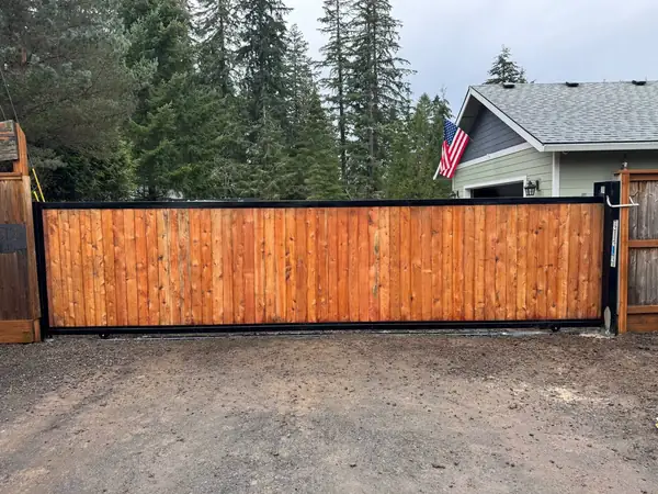 Completed cedar sliding driveway gate with black steel frame, straight-on view