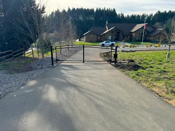Closed arched black metal driveway gate viewed from road, craftsman estate beyond