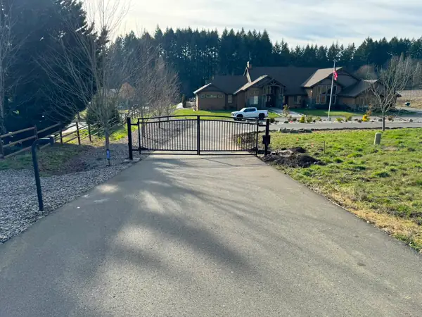 Closed arched black metal driveway gate with estate home and flag in background