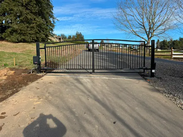 Closed dual-swing black metal driveway gate with LiftMaster operators, blue sky