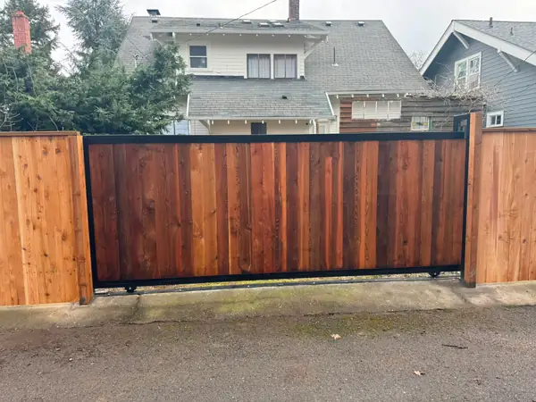 Completed cedar slide gate with steel frame on residential alley, houses behind
