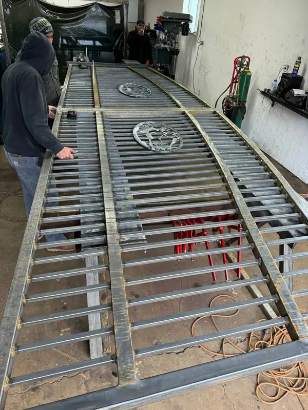 Fabricators building a custom steel driveway gate with decorative medallions in the workshop