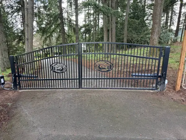 Custom black wrought iron double swing gate with elk medallions and automatic operators on a wooded driveway