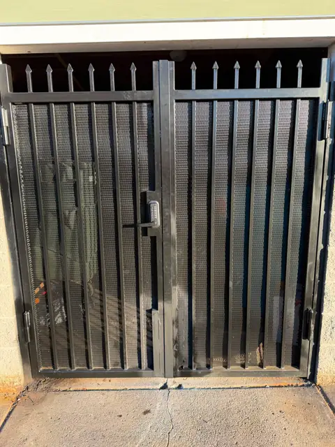 Double black metal security gate with mesh infill and keypad lock at building enclosure