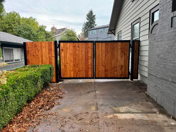 Double cedar swing driveway gate with black steel frame between houses