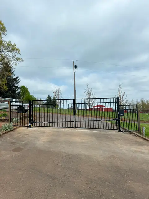 Finished black double-swing driveway gate with operators at rural property