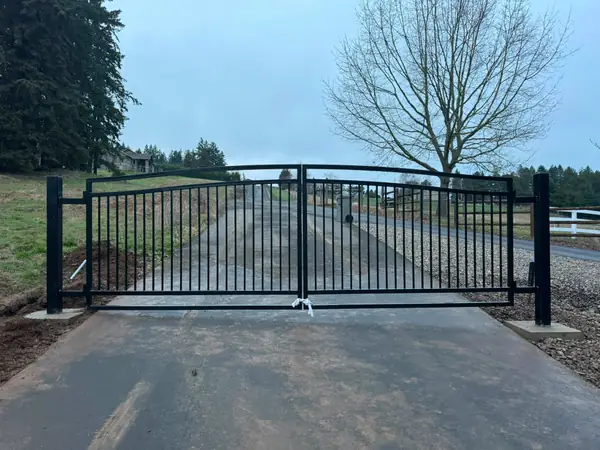 Finished black metal arched double swing driveway gate closed, wide frontal view