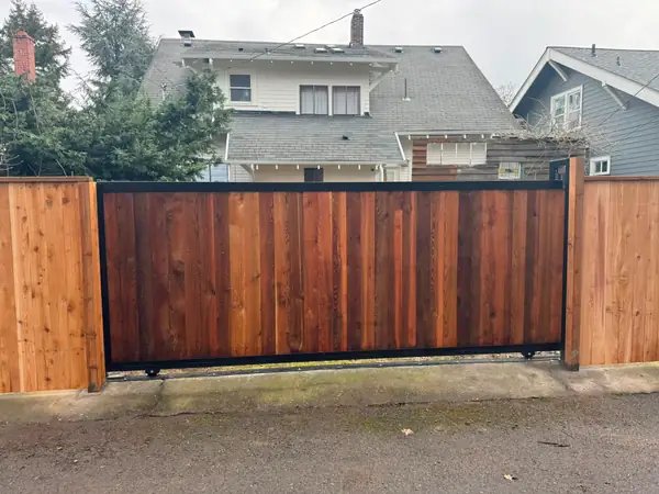 Finished cedar-clad rolling slide gate with black steel frame between wood fence panels in alley