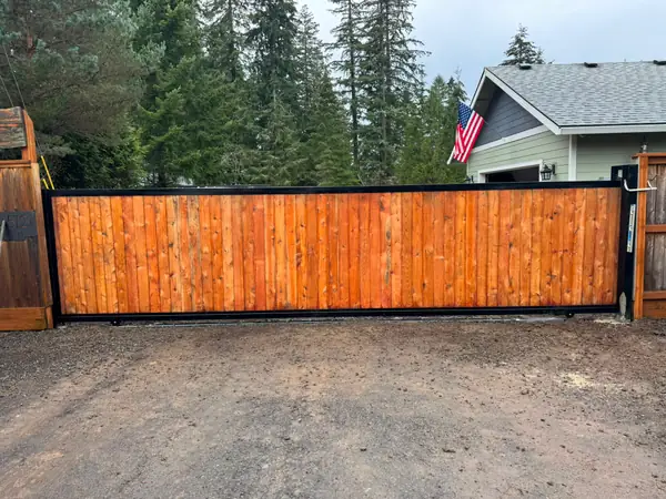 Finished cedar-infill black-steel rolling driveway gate at wooded rural home