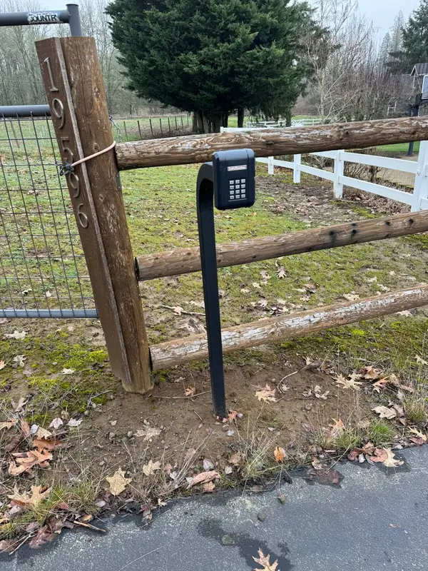 Gate entry keypad mounted on a gooseneck post at a rural driveway