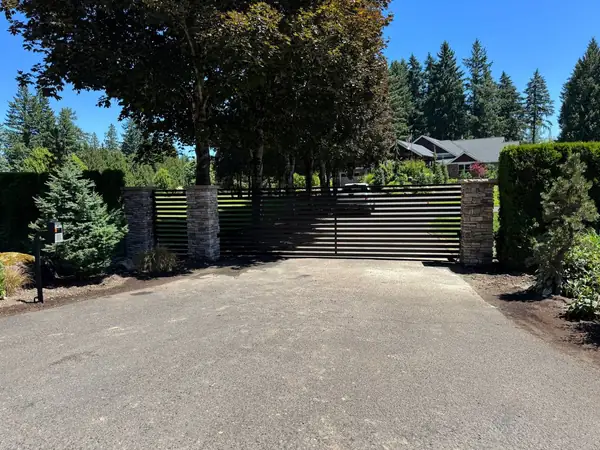 Full driveway entrance with automatic sliding gate, stone pillars, and keypad entry pedestal