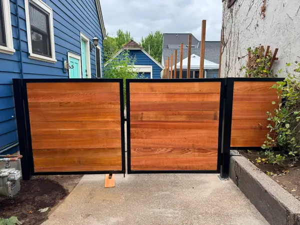Horizontal cedar wood swing gates with black steel frames between houses