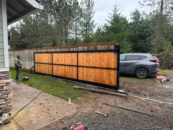 Sliding cedar gate rolled open mid-install with worker and SUV in driveway