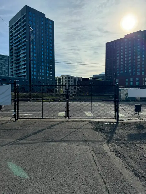 Wide shot of closed black chainlink double gate across urban lot entrance with operators