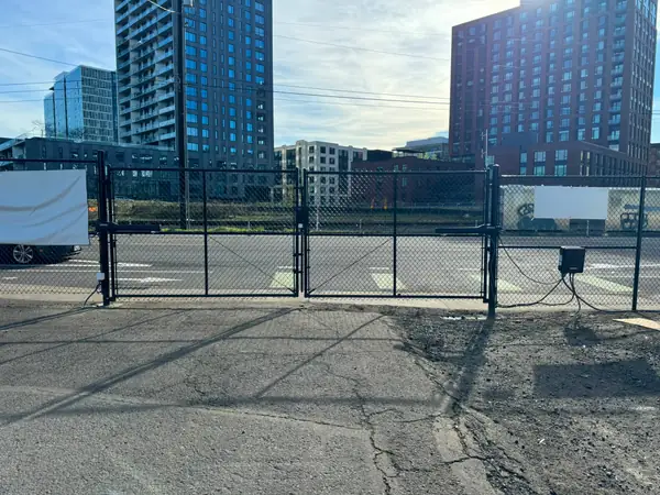 Wide view of black chainlink double swing gate with operators across urban driveway